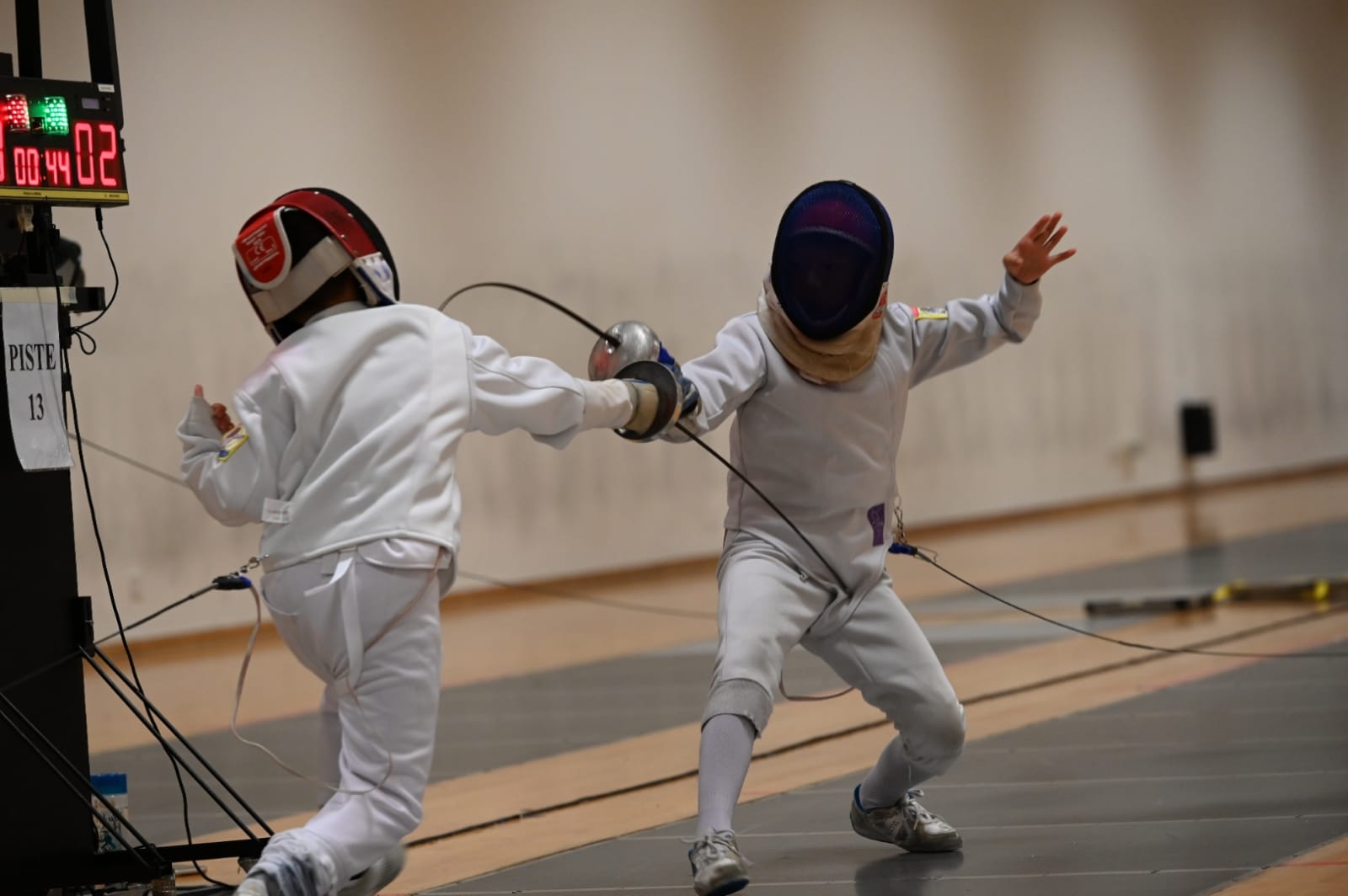 Two young fencers mid-bout on piste 13, one landing a hit as the other extends
