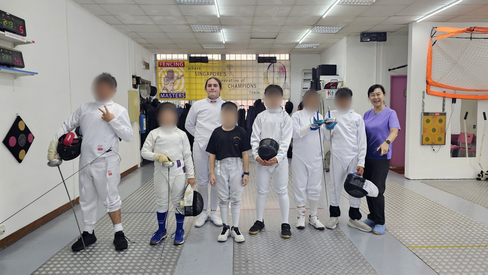 A group of young Fencing Masters fencers in kit with their coaches in the salle at Ubi