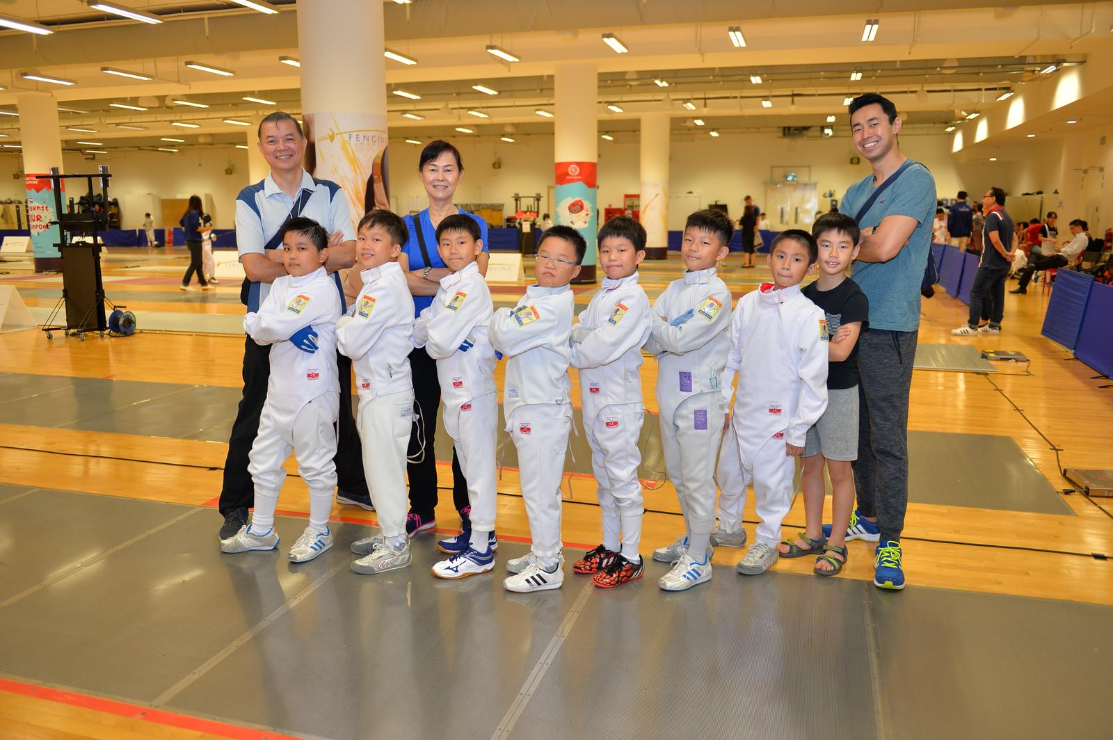 Jeffrey, Lois and Shaun-Paul Lopez with eight young Fencing Masters fencers in jackets at a competition venue
