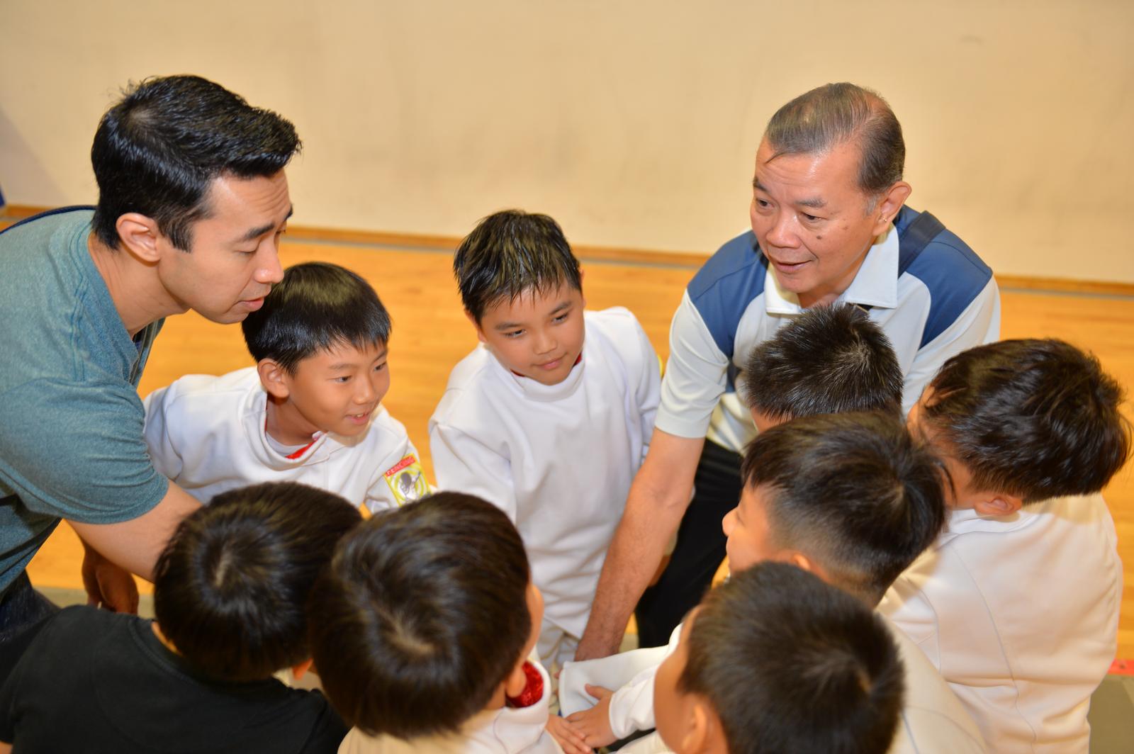 Jeffrey and Shaun-Paul Lopez crouched in a huddle with young fencers, hands together in the middle