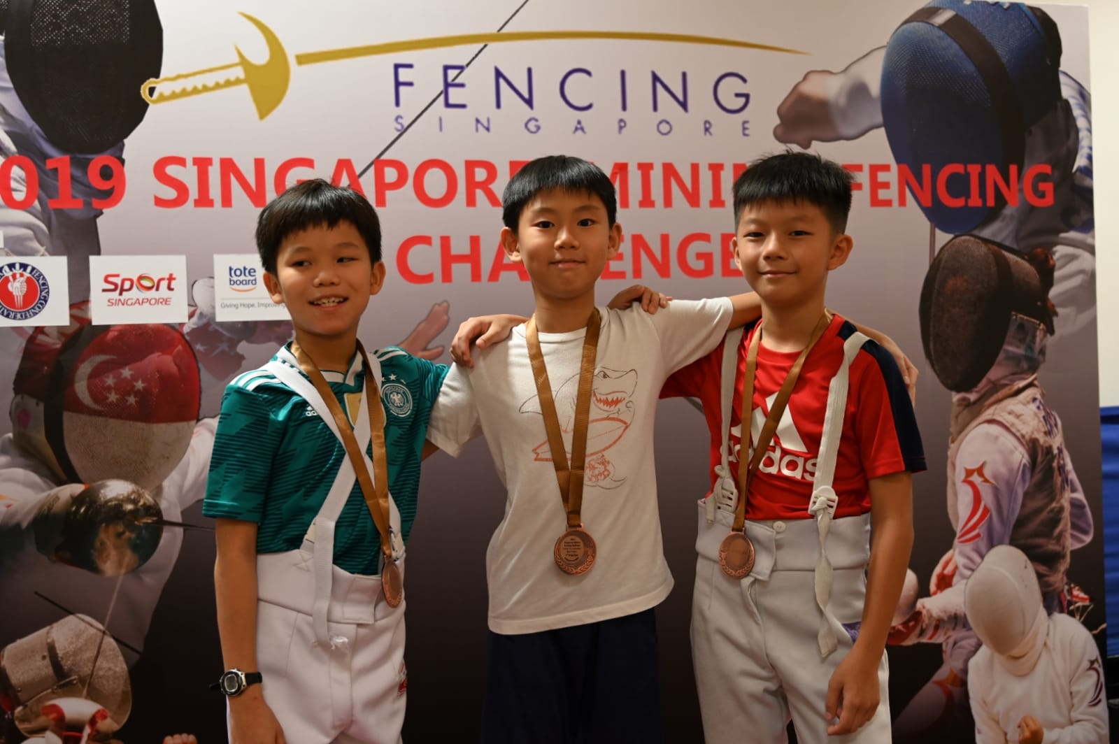 Three young Fencing Masters fencers with bronze medals in front of a Fencing Singapore backdrop