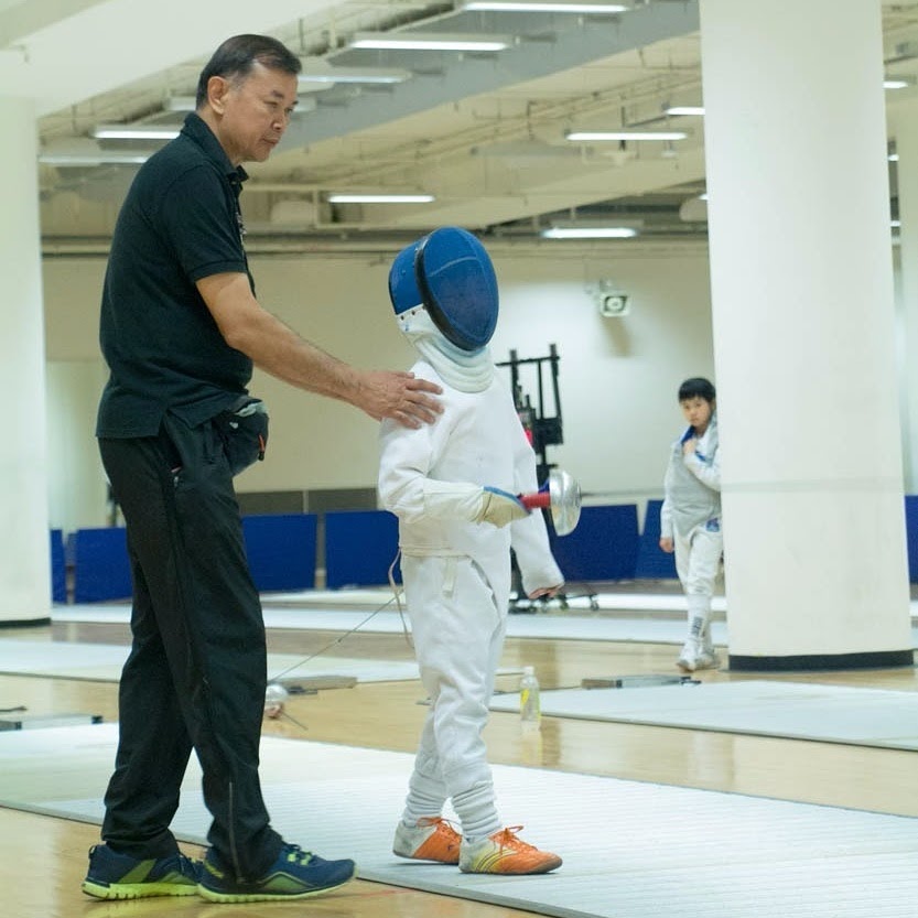 Coach Jeffrey Lopez with a hand on the shoulder of a young fencer in full kit, steadying them before a bout
